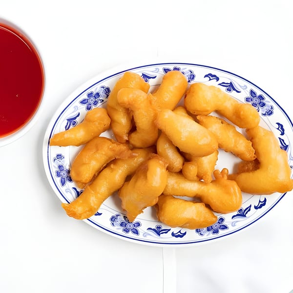 Golden-brown sweet and sour chicken pieces on a blue and white patterned plate with red sauce.