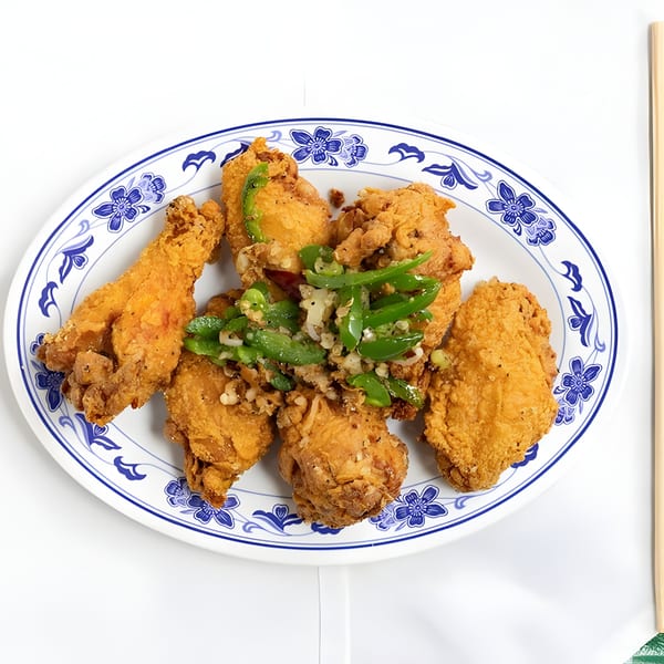 Crispy fried chicken pieces topped with green peppers and garlic on a blue and white patterned plate.