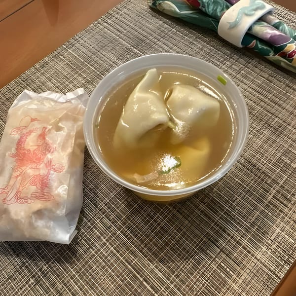 Wonton soup in a white bowl next to a fortune cookie bag on a placemat at Mandarin Cafe.