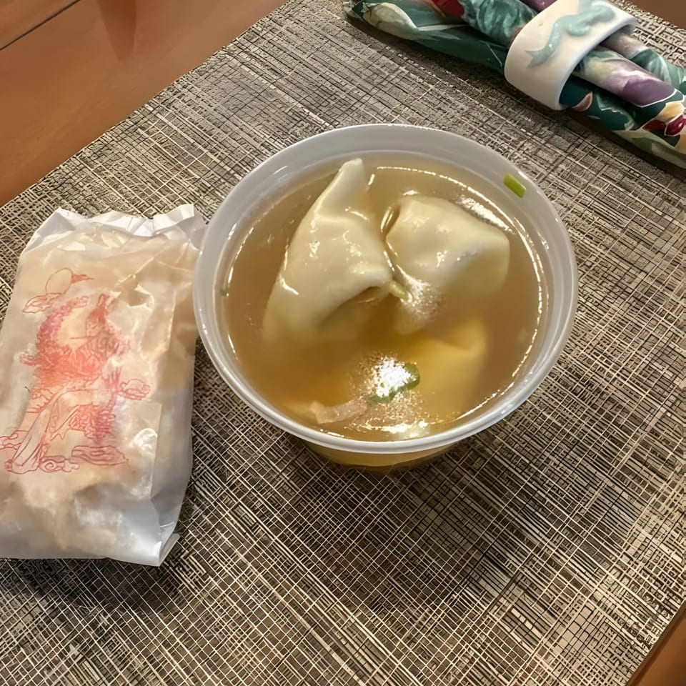 Wonton soup in a white bowl next to a fortune cookie bag on a placemat at Mandarin Cafe.