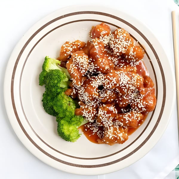 Sesame chicken with broccoli on a white plate with brown stripes, chopsticks on the side.
