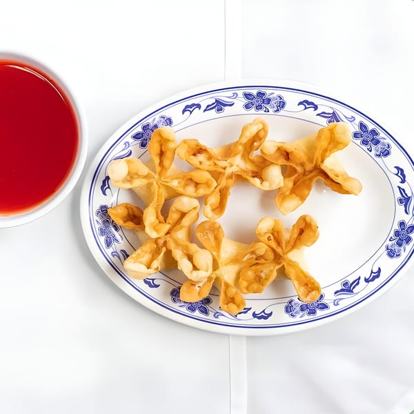 Crab rangoons on a blue and white patterned plate with a side of red dipping sauce.