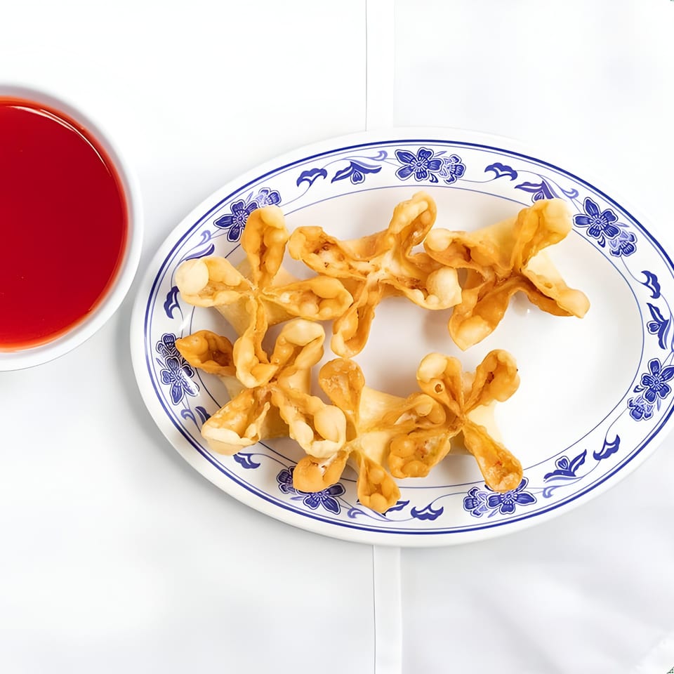 Crab rangoons on a blue and white patterned plate with a side of red dipping sauce.